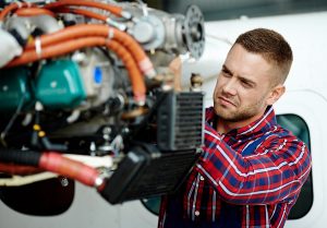 aircraft mechanic in a red plaid shirt working on an engine