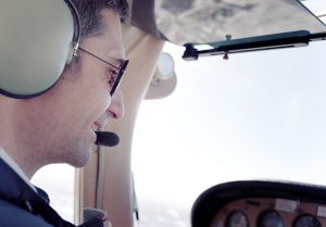 smiling pilot flying a plane while wearing headset and sunglasses